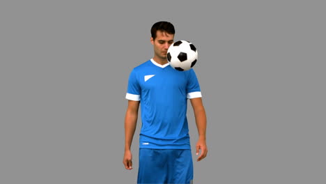 Man-juggling-a-football-with-his-knee-on-grey-screen