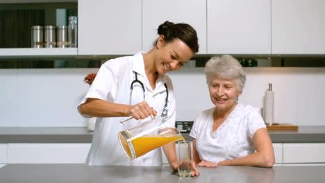 Home-nurse-pouring-orange-juice-for-patient-in-kitchen