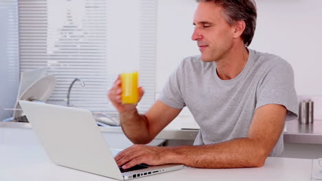 Reifer-Mann-Trinkt-Orangensaft,-Während-Er-Seinen-Laptop-Benutzt