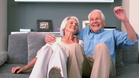 Retired-couple-sitting-down-on-the-couch-and-smiling