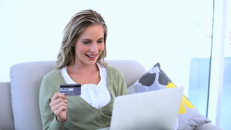 Delighted-woman-holding-her-credit-card-and-using-her-laptop