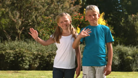 Cheerful-siblings-waving-together-in-their-garden