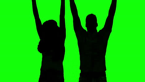 Silhouette-of-couple-jumping-and-raising-arms-on-green-screen