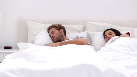 Couple-sleeping-peacfully-with-partner-pressing-snooze