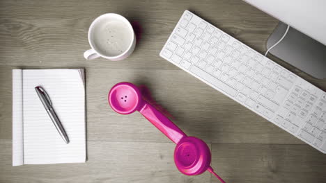Pink-phone-receiver-falling-onto-office-desk