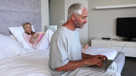 Couple-relaxing-in-bed-and-man-doing-his-own-thing