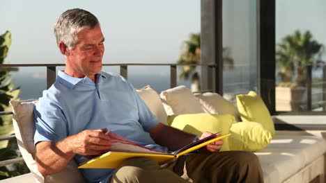 Mature-man-looking-at-picture-album-on-the-balcony