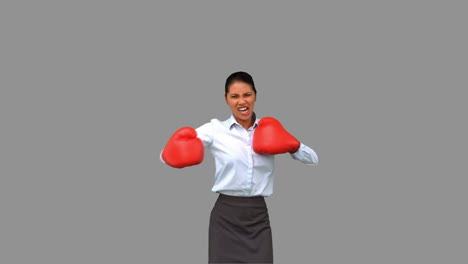 Businesswoman-gesturing-with-boxing-gloves-on-grey-screen