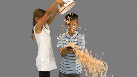 Sister-pouring-popcorn-on-brothers-head-on-grey-screen