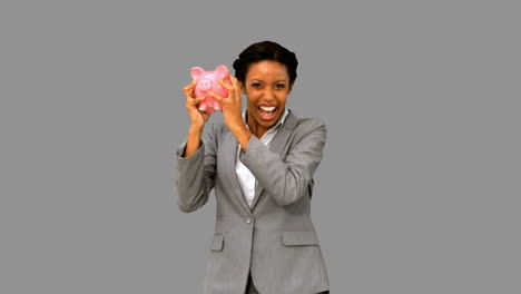 Businesswoman-listening-to-a-full-piggy-bank-on-grey-screen
