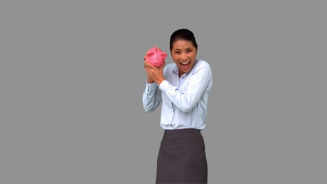 Businesswoman-shaking-a-full-piggy-bank-on-grey-screen