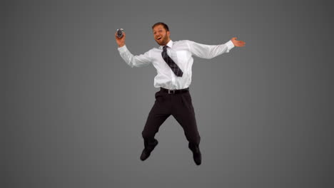 Businessman-holding-alarm-clock-jumping-on-grey-background