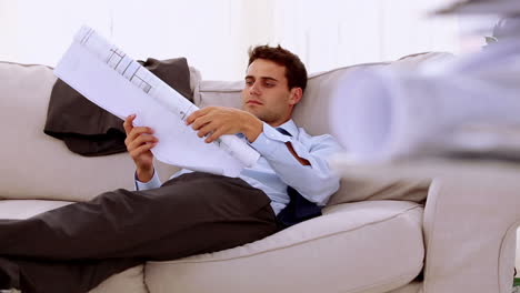 Businessman-lying-on-couch-and-looking-at-a-document-