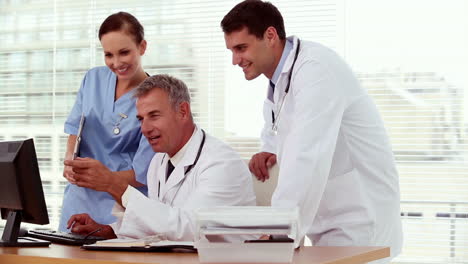 Smiling-doctor-showing-something-to-his-colleagues-on-his-computer-