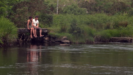 Couple-sitting-by-a-lake-and-dangling-their-legs