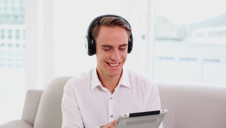 Amused-cute-man-listening-to-music-while-using-his-tablet