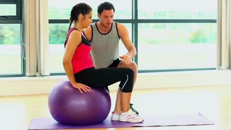 Hübsche-Frau-Beim-Training-Auf-Fitness-Ball-Mit-Trainer-Sitzen