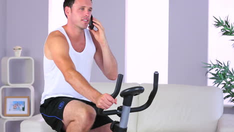 Attractive-sporty-man-exercising-on-bike-and-phoning
