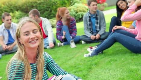 Blonde-student-smiling-at-camera-with-friends-behind-her-on-grass