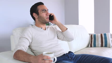 Handsome-man-answering-the-phone-while-relaxing-on-his-sofa