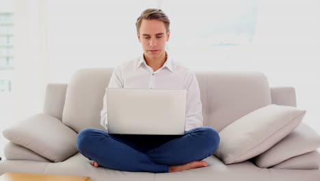 Handsome-young-man-sitting-concentrated-on-couch-using-his-notebook