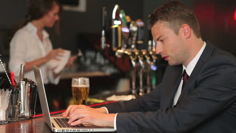 Serious-businessman-working-on-his-laptop-while-drinking-beer