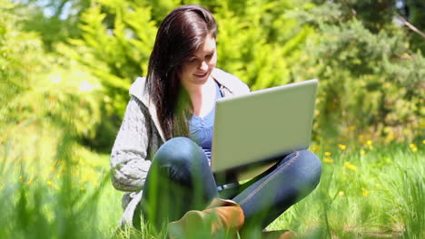 Happy-young-woman-sitting-on-grass-using-laptop