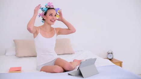 Young-model-in-hair-rollers-using-her-digital-tablet-to-video-chat-on-her-bed