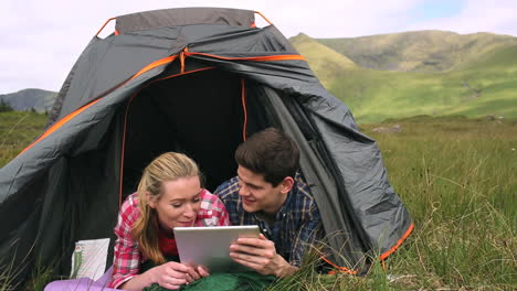 Happy-couple-using-a-digital-tablet-lying-in-their-tent