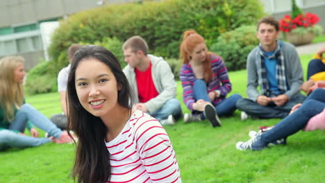 Studentin-Lächelt-In-Die-Kamera-Mit-Freunden-Hinter-Ihr-Auf-Dem-Rasen