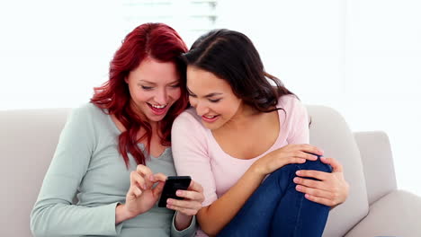 Überraschende-Süße-Frauen,-Die-Ein-Smartphone-Benutzen,-Während-Sie-Auf-Der-Couch-Sitzen