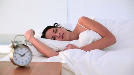 Brunette-being-woken-by-her-alarm-clock-in-bed