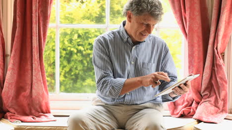 Mature-man-sitting-by-a-window-using-his-laptop
