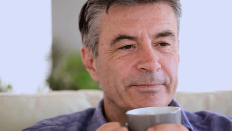 Happy-mature-man-relaxing-on-his-couch-drinking-coffee