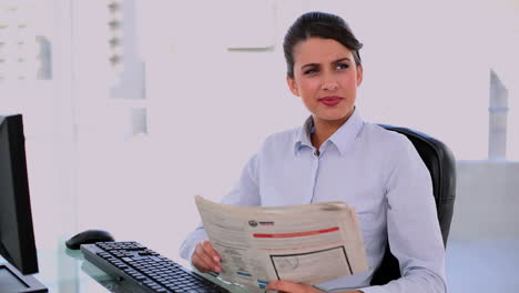 Thoughtful-beautiful-businesswoman-using-computer-while-reading-newspaper