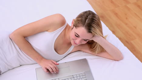 Happy-gorgeous-blonde-lying-on-bed-using-laptop