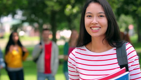 Student-smiling-and-waving-at-camera-with-friends-standing-behind-her