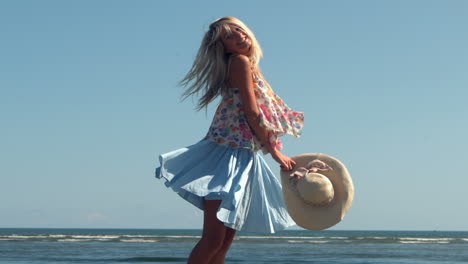 Attractive-blonde-holding-straw-hat-spinning-on-beach