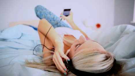 Attractive-blonde-lying-on-her-back-on-bed-listening-to-music