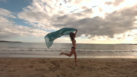 Woman-running-at-the-beach-holding-a-scarf