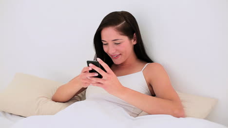 Attractive-brunette-texting-on-her-smartphone-in-bed