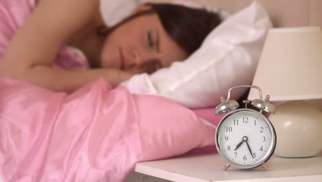 Alarm-clock-ringing-and-waking-a-sleeping-woman