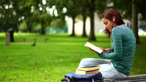 Pretty-student-sitting-on-bench-reading-a-book