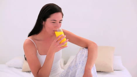 Attractive-brunette-drinking-a-glass-of-orange-juice-in-bed