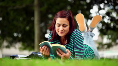 Pretty-student-lying-on-grass-reading-a-book-listening-to-music