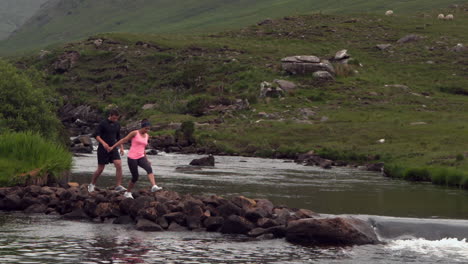 Pareja-Cruzando-Rocas-En-Medio-De-Un-Río-Que-Fluye