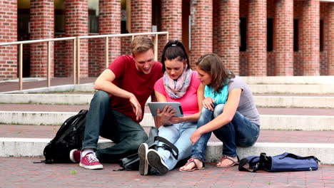 Happy-students-using-tablet-outside-on-steps