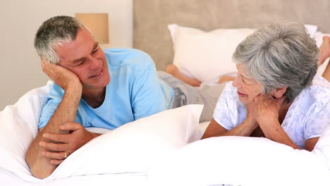 Happy-senior-couple-lying-on-bed-chatting