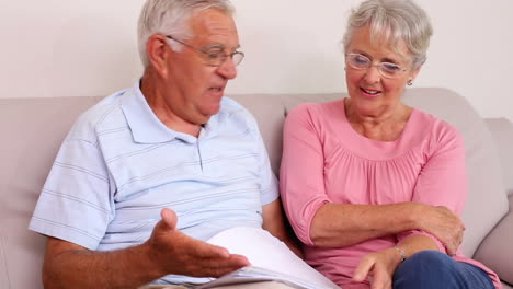 Senior-couple-sitting-on-sofa-reading-documents