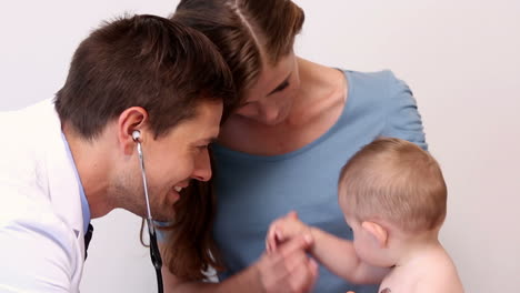 Pretty-mother-holding-baby-boy-while-pediatrician-listens-to-his-chest